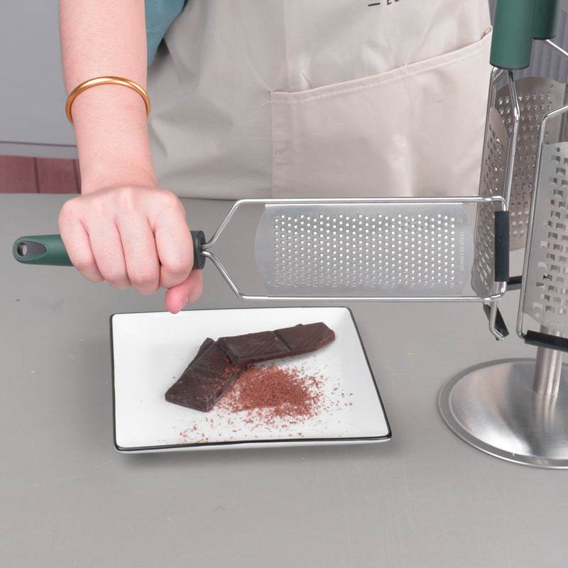 Person using a stainless steel cheese grater on a piece of chocolate in a modern kitchen.