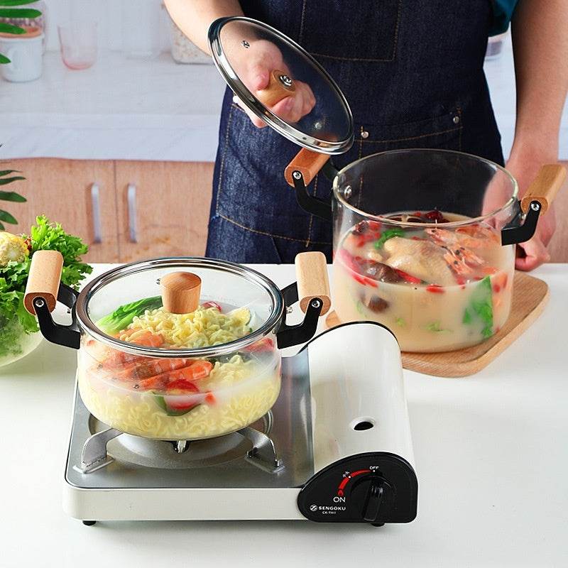 Borosilicate Visions Cookware Pot with wooden handles, cooking on a stovetop with visible ingredients.