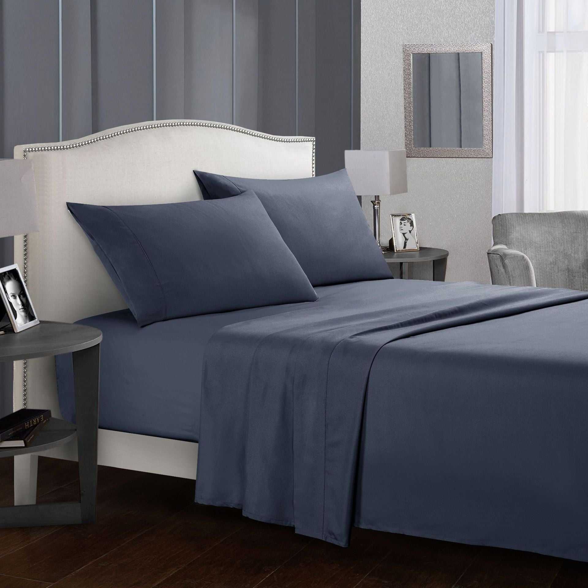 Four-piece bed sheet set in dark gray with pillows on a neatly made bed.