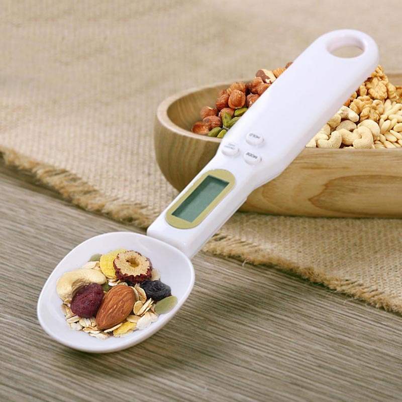 White LCD digital kitchen scale spoon measuring nuts and oats.