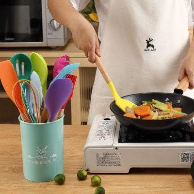 Silicone kitchenware set with wooden handles in use for cooking vegetables.