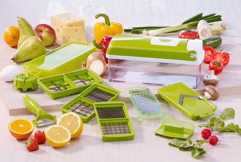 Multifunctional vegetable chopper with various blades and accessories on a kitchen counter with fruits and vegetables. 