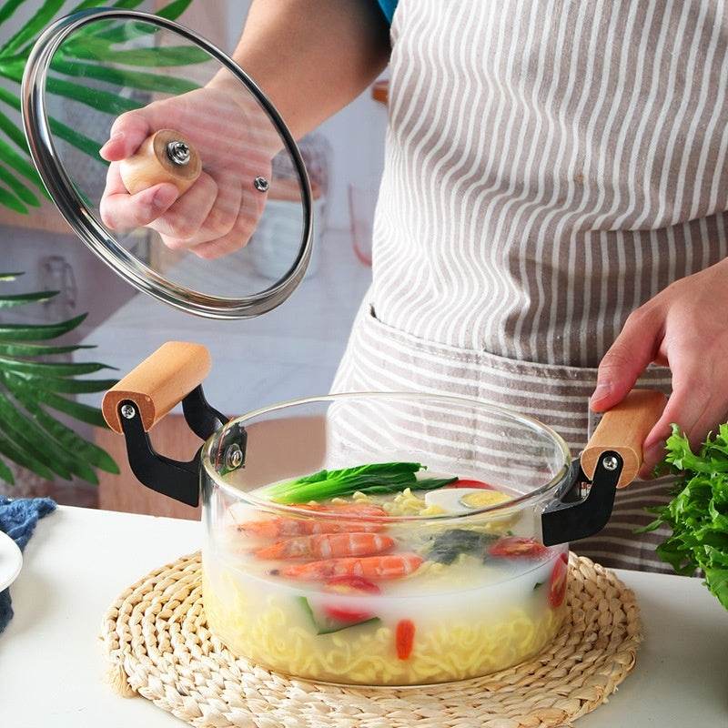 Borosilicate Visions Cookware Pot with wooden handles and glass lid, filled with soup and vegetables.