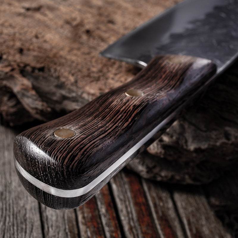 Close-up of a hand-forged stainless steel knife with a chicken wing wood handle and copper nails, resting on a wooden surface.