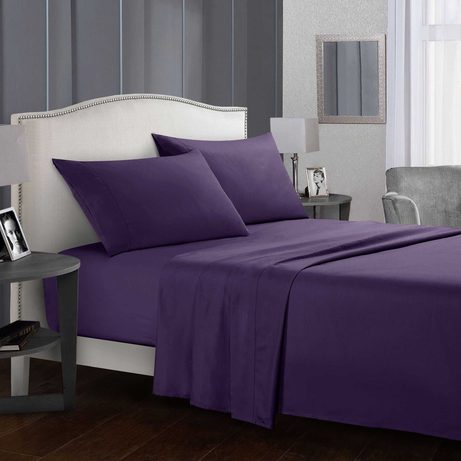 Four-piece bed sheet set on a modern bed with purple sheets and pillows.