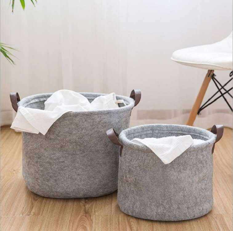 Large and medium gray felt sundry storage baskets with handles on wooden floor.