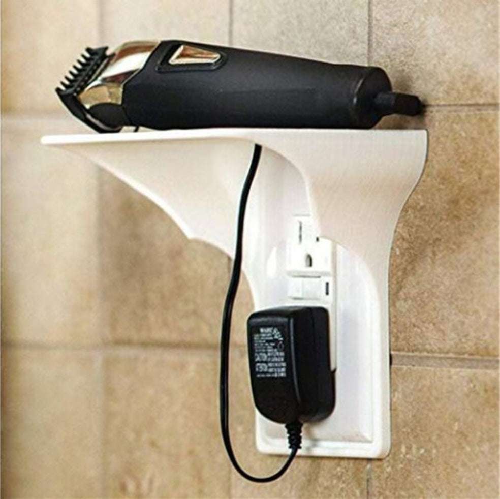 Wall outlet organizer with white shelf holding grooming device, installed without drilling, tidy cable management.