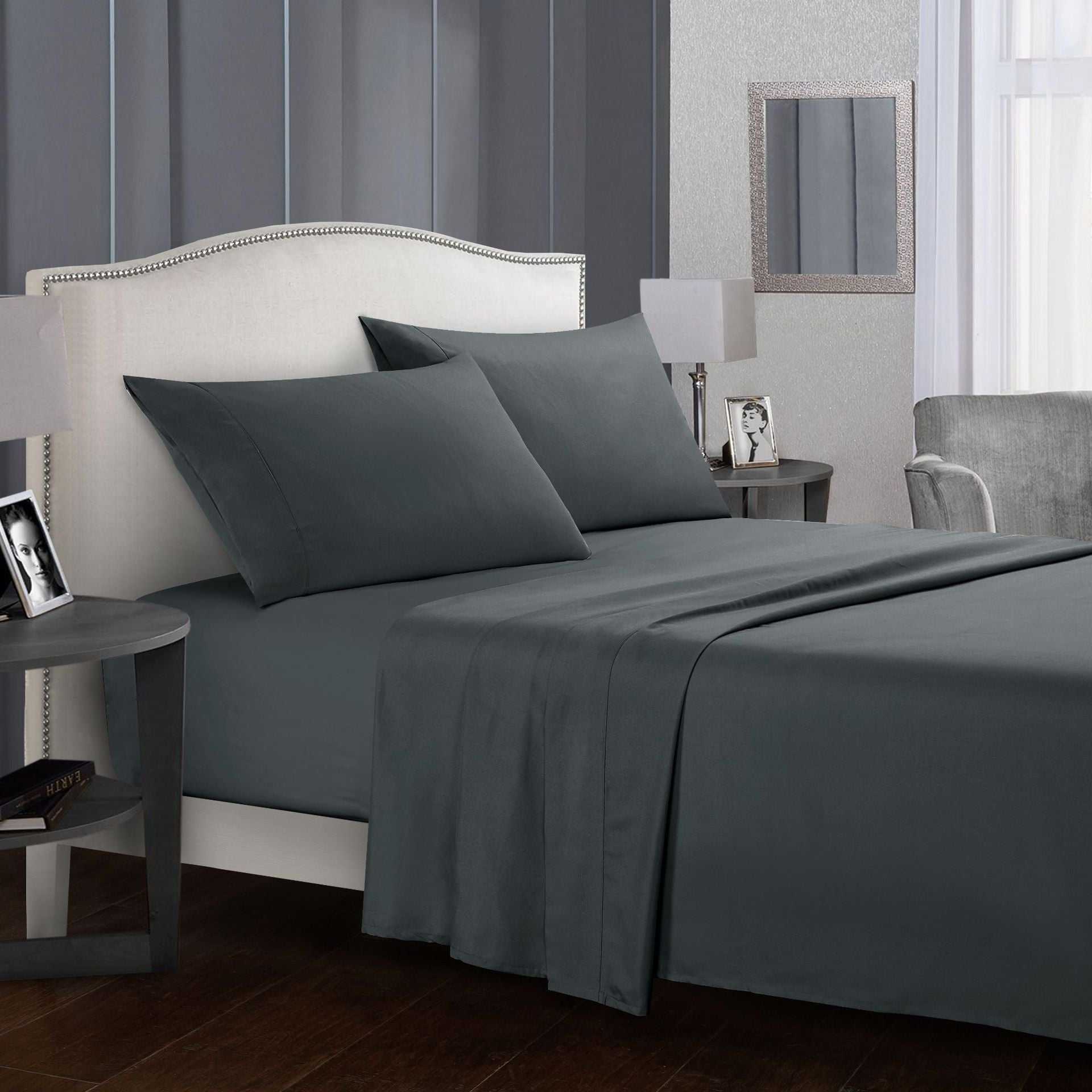 Four-piece bed sheet set in dark tone on a neatly arranged bed with pillows.