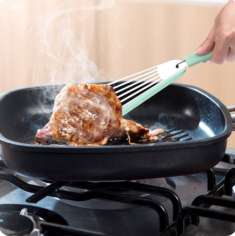 Nonstick fish spatula flipping food in a frying pan on a stove.