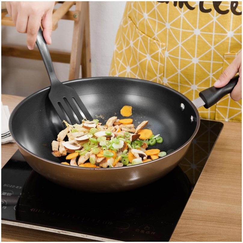 Cooking vegetables in a black non-stick cast iron wok from a light luxury cookware set.