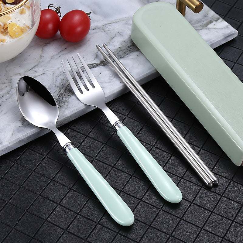 Portable Nordic tableware set in stainless steel with light green handles, including a spoon, fork, and chopsticks, on a textured surface.