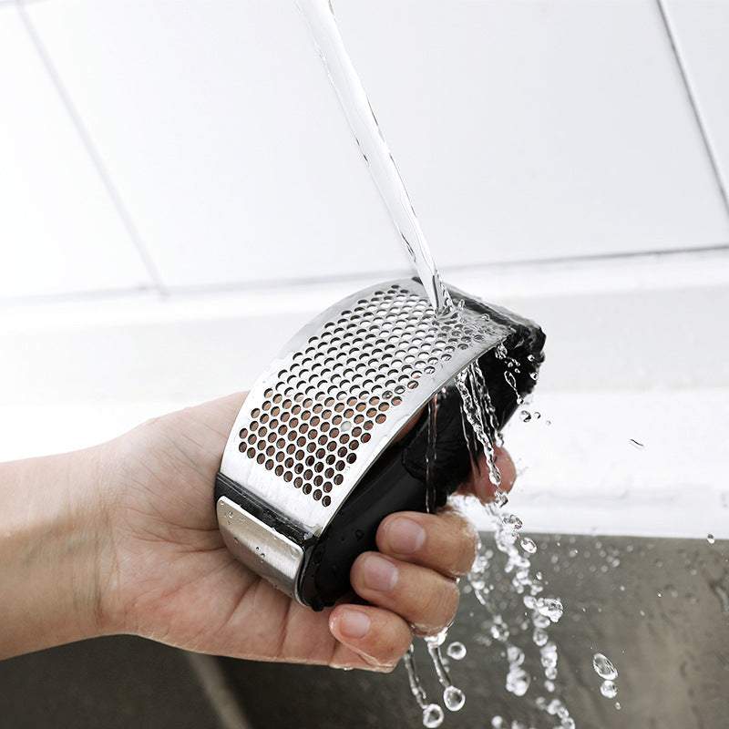 Stainless steel garlic press being rinsed under running water.