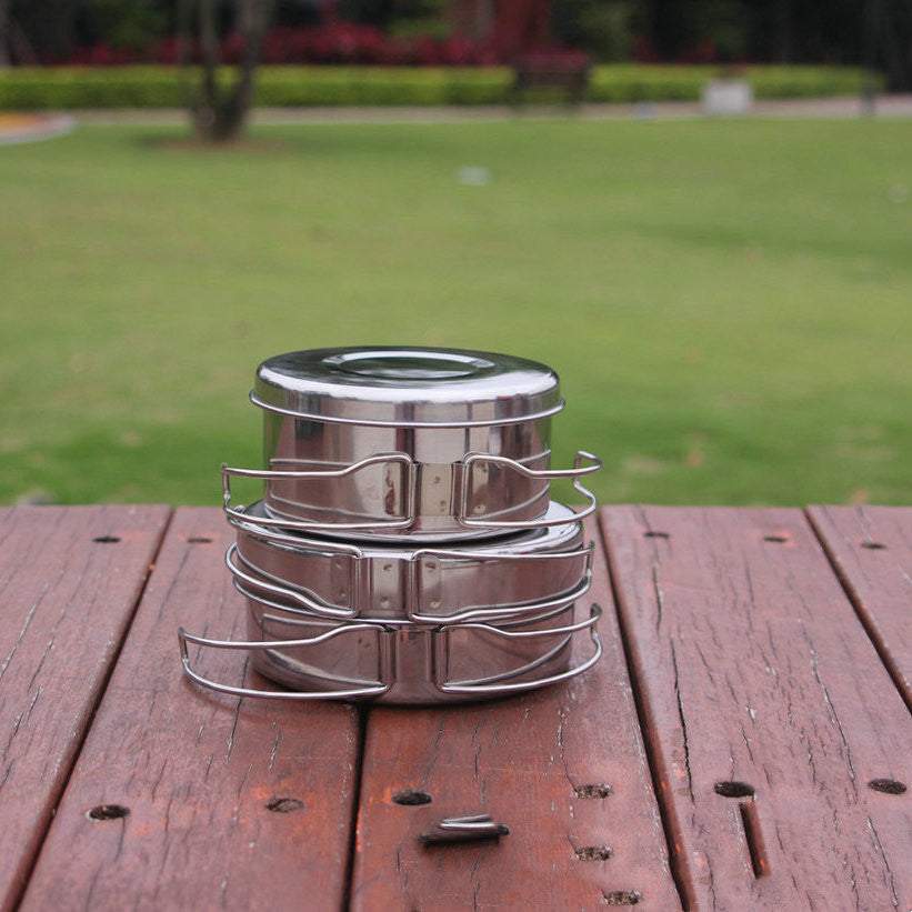 Outdoor stainless steel cookware set on wooden surface.