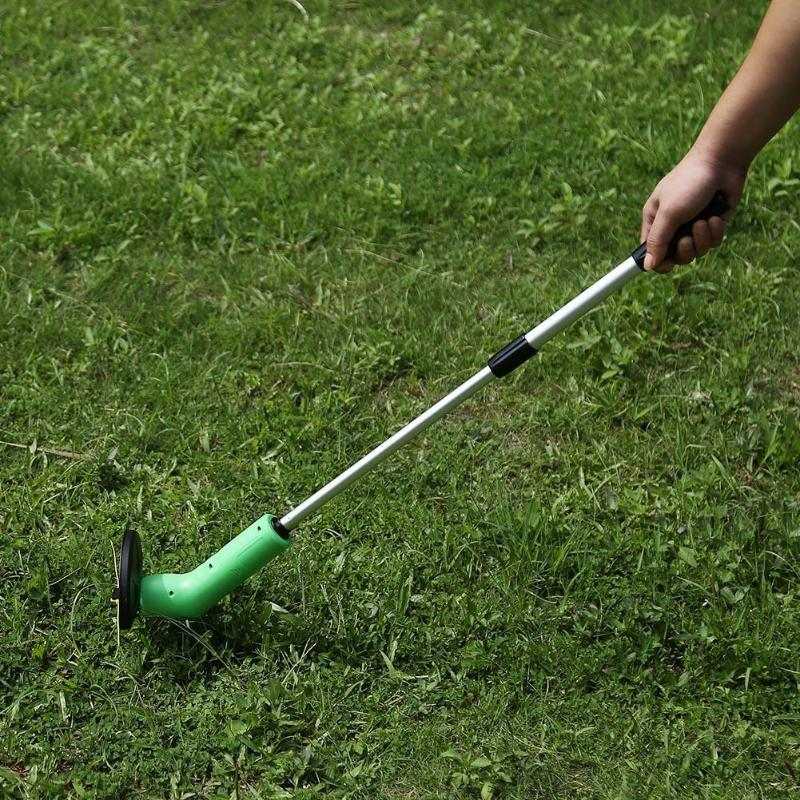 Cordless lawn trimmer with extension pole trimming grass.
