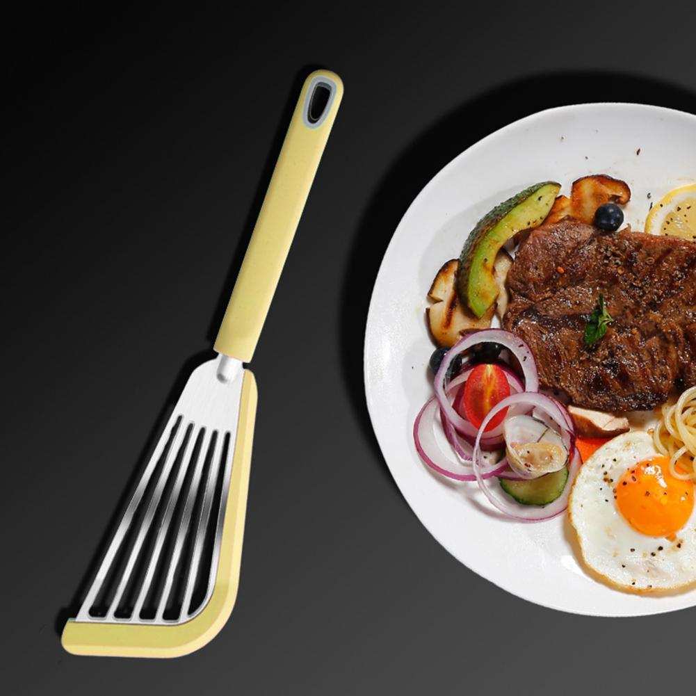 Nonstick fish spatula with a silicone handle and wide slotted blade, ideal for flipping fish, eggs, and pancakes; shown next to a plate of food.