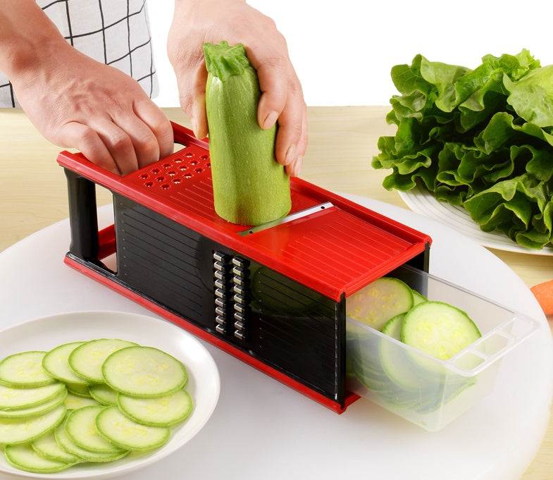Multifunctional kitchen utensil cutting tool with red and black design, slicing zucchini with added drain storage box.