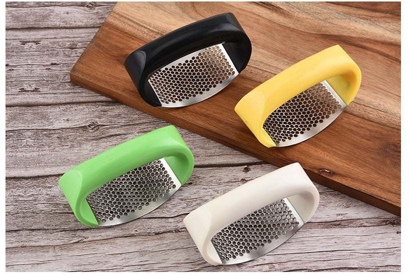Stainless steel garlic press with ergonomic ABS handles in multiple colors on a wooden surface.
