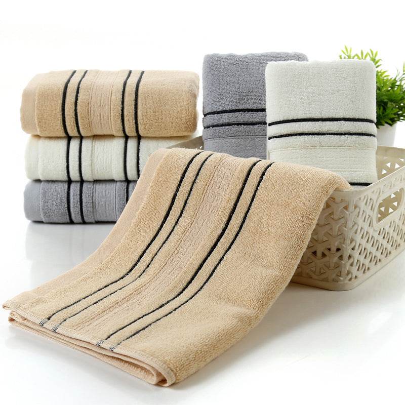 Household pure cotton towels in beige, gray, and white neatly stacked in a basket, showcasing their soft and absorbent texture.