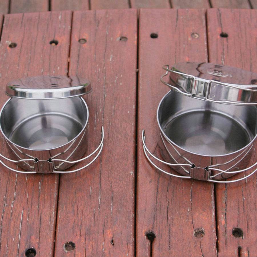 Outdoor stainless steel cookware set for camping on a wooden surface.