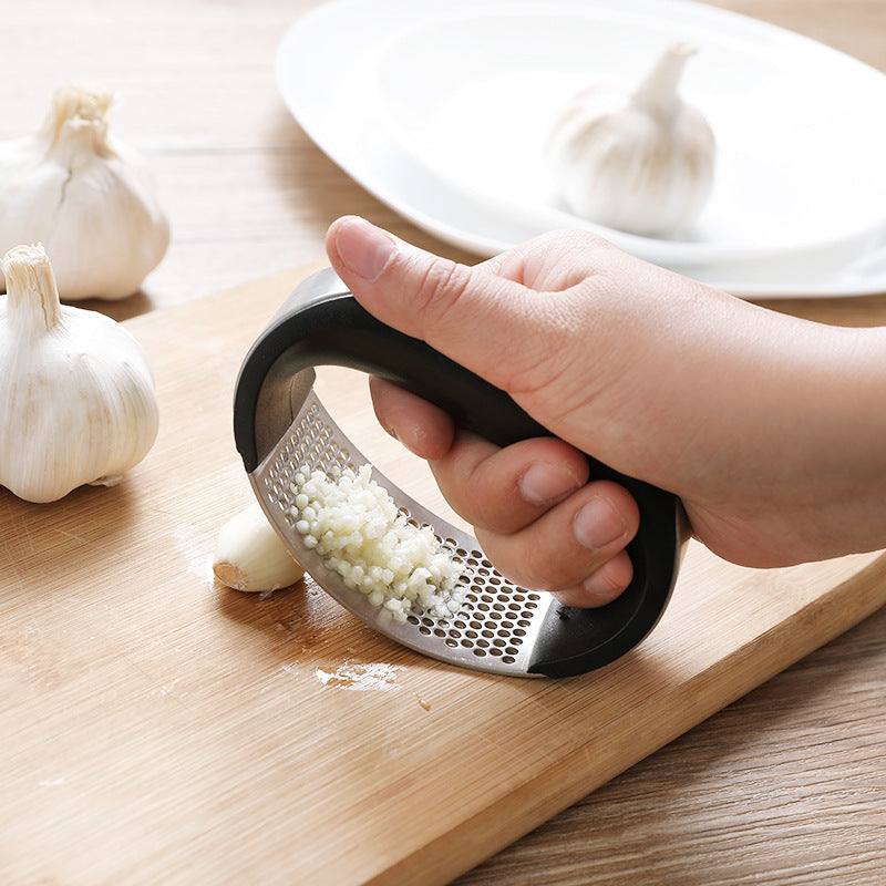 Stainless steel garlic press being used to mince garlic cloves on a wooden cutting board.