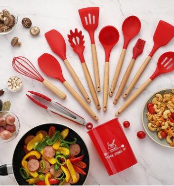 Red silicone kitchenware set with wooden handles on a countertop with food.