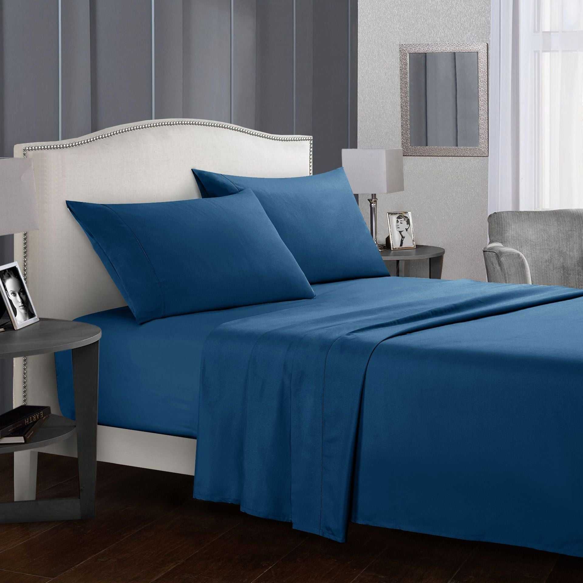 Blue four-piece bed sheet set on a bed with matching pillows in a modern bedroom.