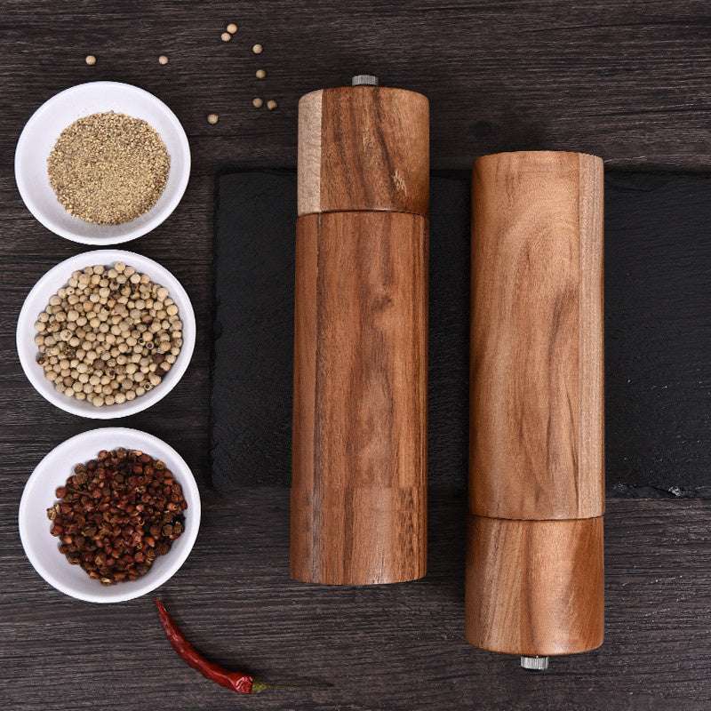Cylindrical acacia wood pepper grinders with ceramic core on a dark surface.