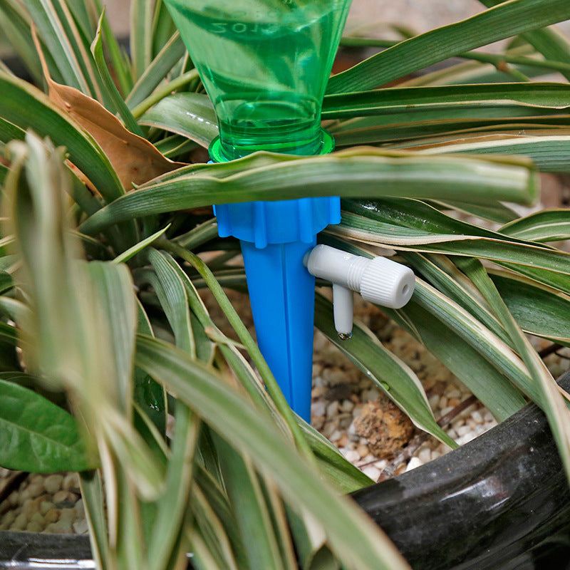 Automatic plant watering spike inserted into soil with a green bottle above, in a potted plant setup.