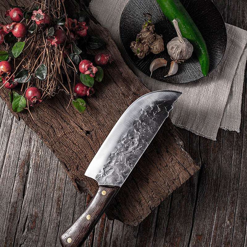 Hand forged stainless steel knife with chicken wing wood handle, displayed on rustic wooden board with fruits and vegetables.
