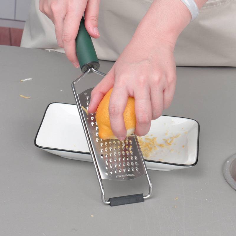 Stainless steel cheese grater being used to grate a lemon over a bowl.