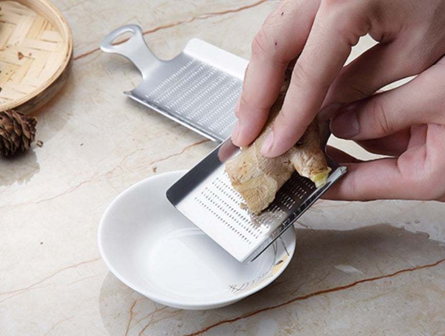 Stainless steel garlic press being used to grate ginger over a dish.