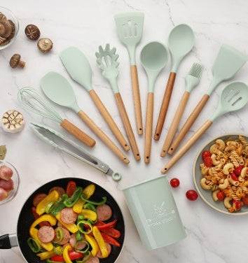 Silicone kitchenware set with wooden handles and various utensils on a marble countertop, surrounded by ingredients.
