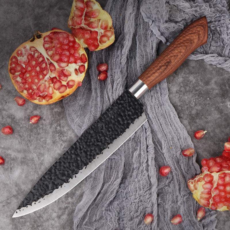 Stainless steel fish fillet slicing knife with wooden handle on textured surface, surrounded by pomegranates.