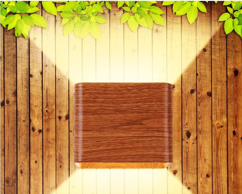Square LED indoor lighting wall lamp in imitation wood finish on wooden background.