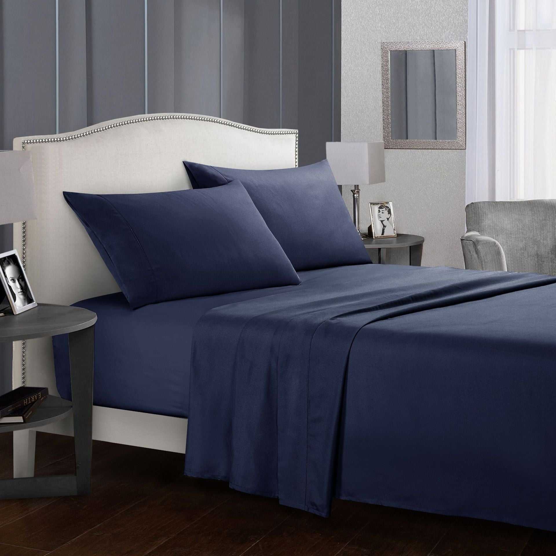 Four-piece bed sheet set in navy blue displayed in a modern bedroom.