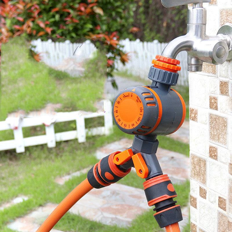 Mechanical timing controller irrigation system attached to outdoor faucet in garden setting.