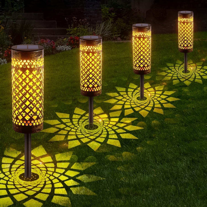 Metal solar-powered lawn lamps with warm light illuminating a garden, featuring geometric abstract art design.