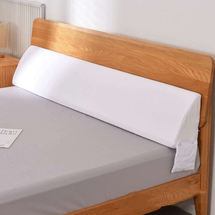Long white pillow wedge filling gap between bed and headboard.
