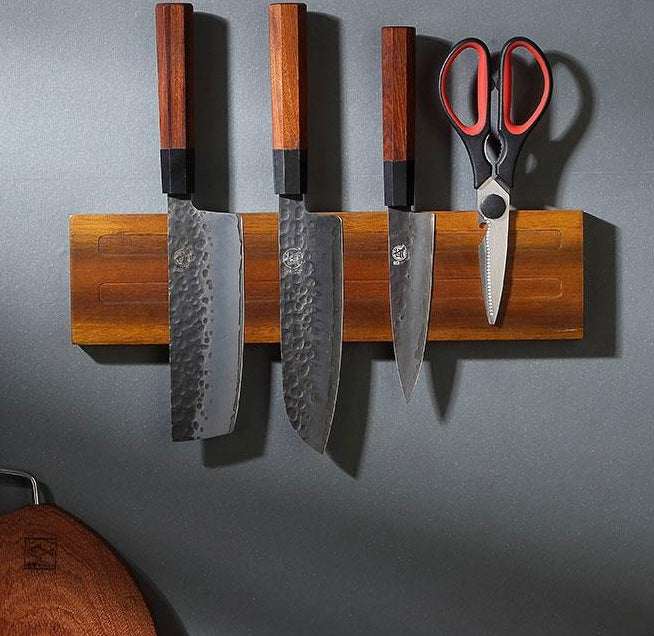 Wall-mounted solid wood magnetic kitchen knife rack holding knives and scissors.