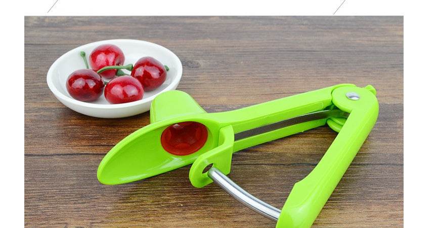 Cherry kernel remover tool in green next to a bowl of red cherries.