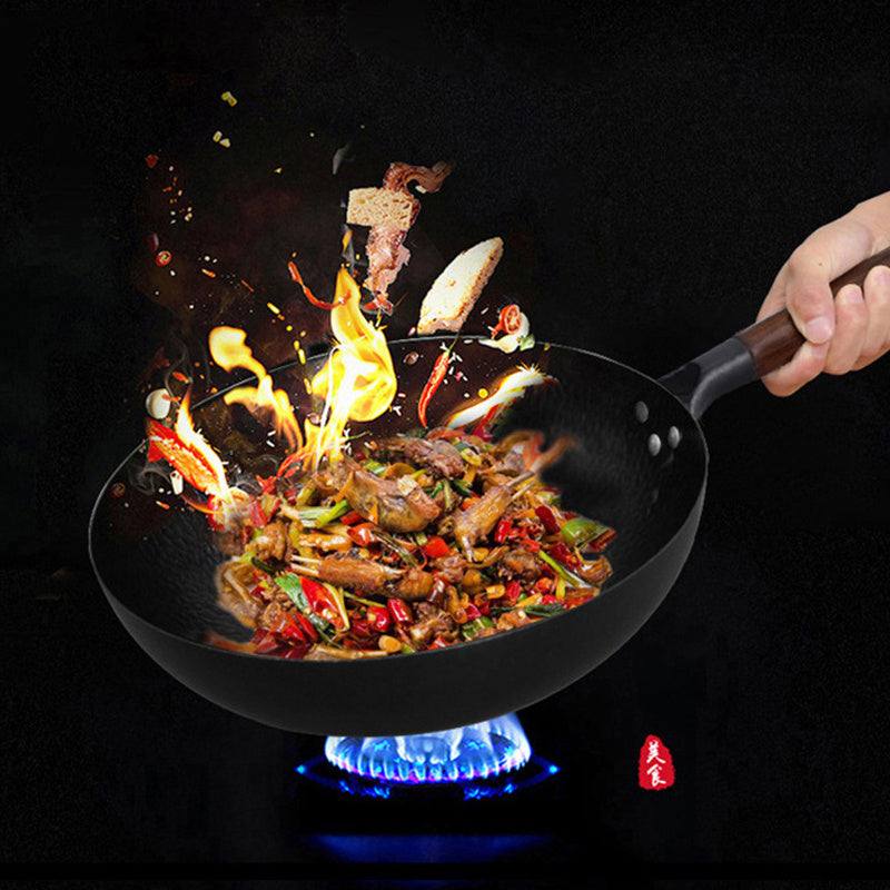 Traditional iron pan capturing vibrant cooking flames with food, featuring a wooden handle on a stovetop.