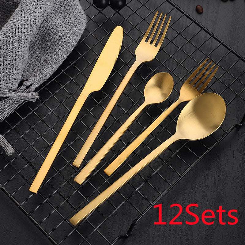 Gold stainless steel cutlery set on black grid with napkin, includes knife, fork, spoon, and tea spoon, labeled "12 Sets".