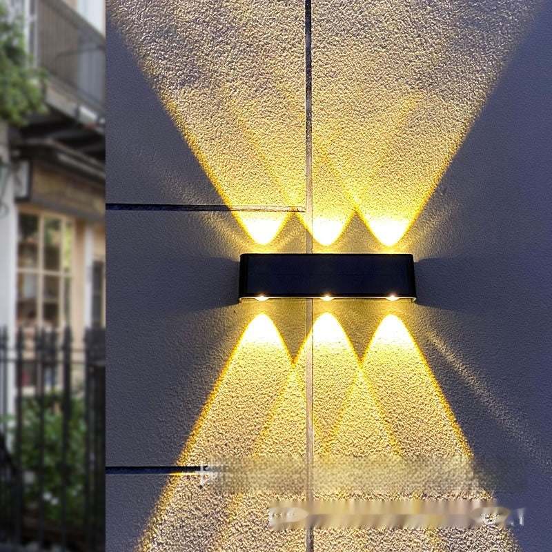 Solar lamp outdoor on wall, illuminating courtyard with warm yellow light.