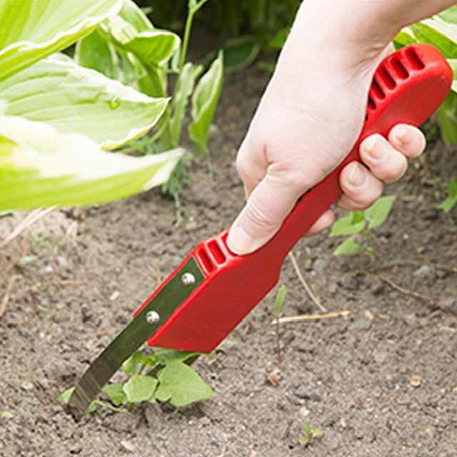 Garden weeding tool with red plastic handle in use among plants.