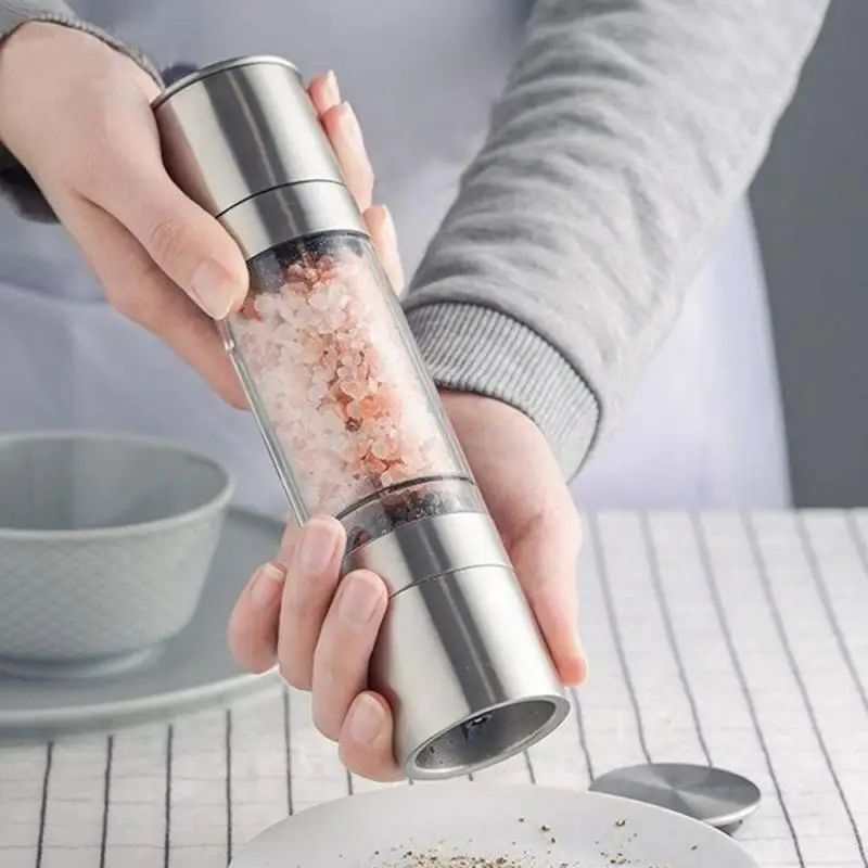 Manual stainless steel salt pepper grinder, double-headed with adjustable ceramic grinding, held in hands.