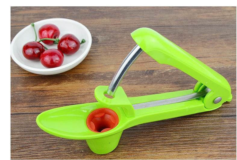 Cherry Red Date Cherry Kernel Remover in green on a wooden table with cherries in a bowl.