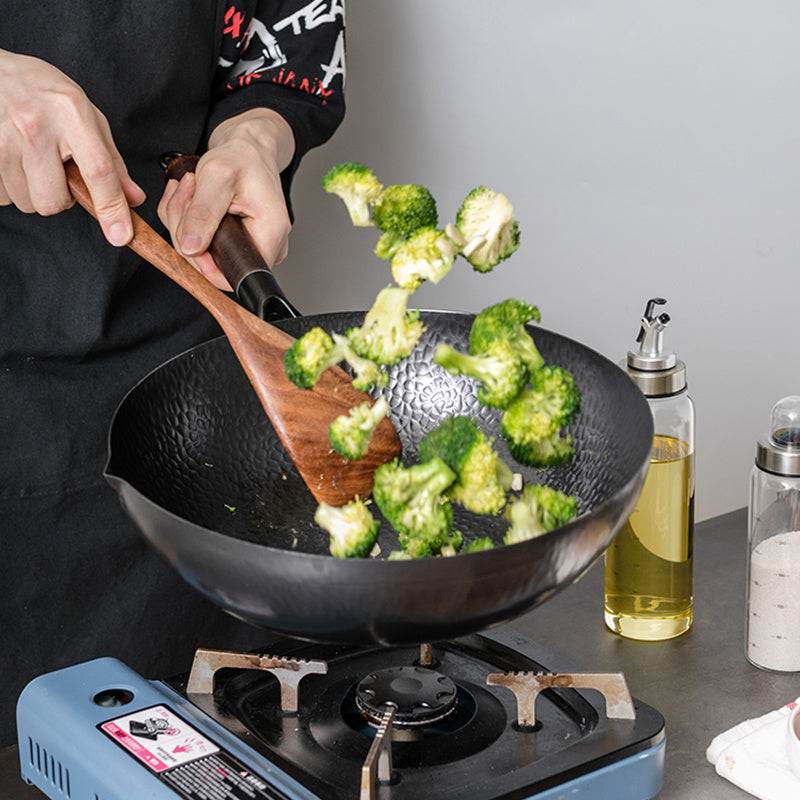 Handmade iron pan used for cooking broccoli on stovetop.