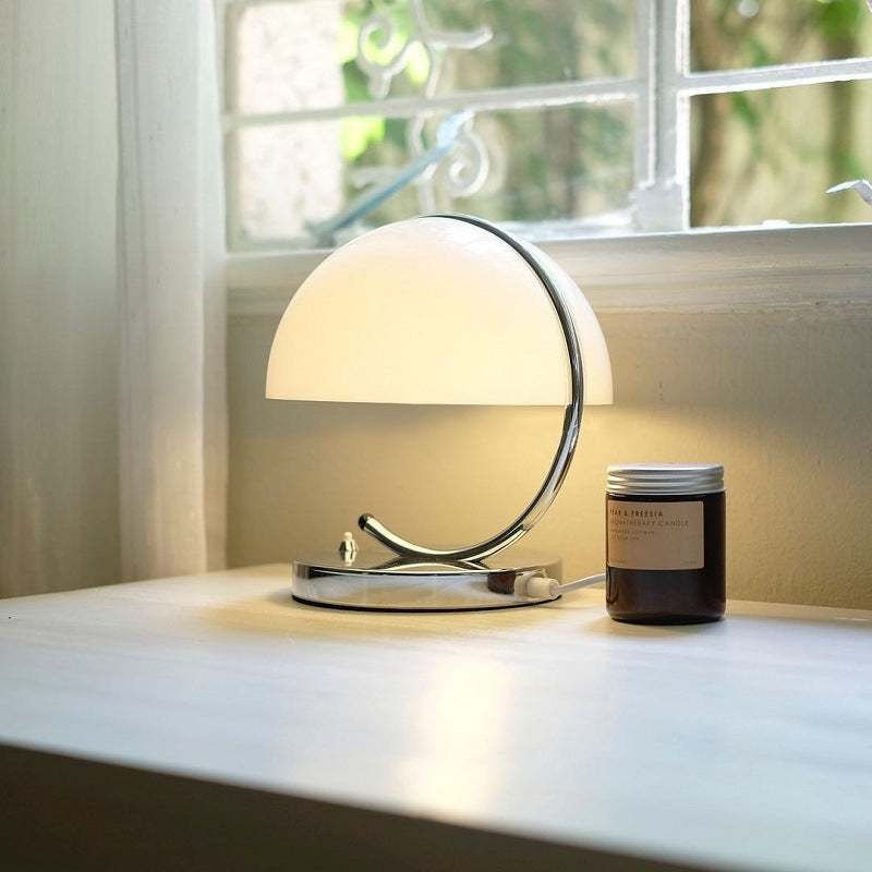 Retro Space Age table lamp with glass shade on a bedside table, emitting warm LED light in a modern living room setting.